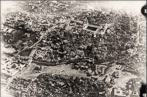 <p>1918’de Medine’nin uçaktan görünüşü. Hazret-i Peygamberin mezarının da bulunduğu Mescid-i Nebevi çevresinde kurulmuş olan Medine de pek çok İslam şehri gibi surlarla çevrilidir. Surların hemen dışında, ortada görülen alan Menaha Meydanı'dır.</p>