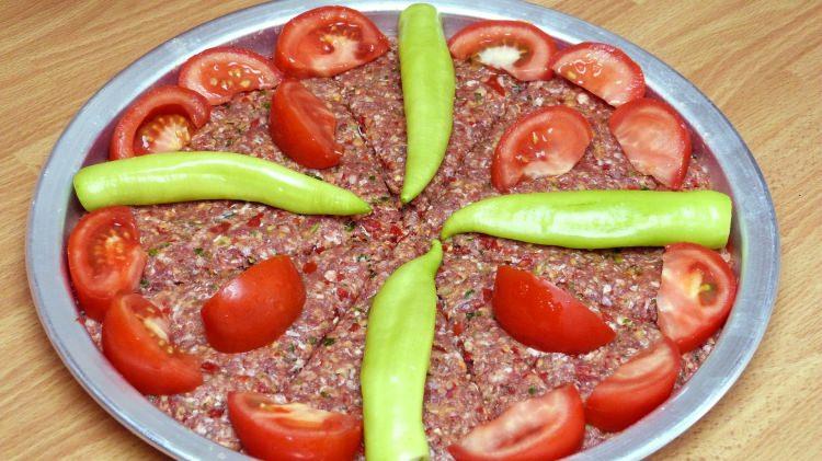<p>Kıyma, tepsi içerisine bastırılarak yayılıyor. Tepsinin boş kalan kısmına halka halka doğranan soğanlar, dilimlenen domates ve biberler diziliyor. Daha sonra tuz serpilen kebap, fırın ocağında pişirilerek hazır hale getiriliyor.</p>

<p> </p>
