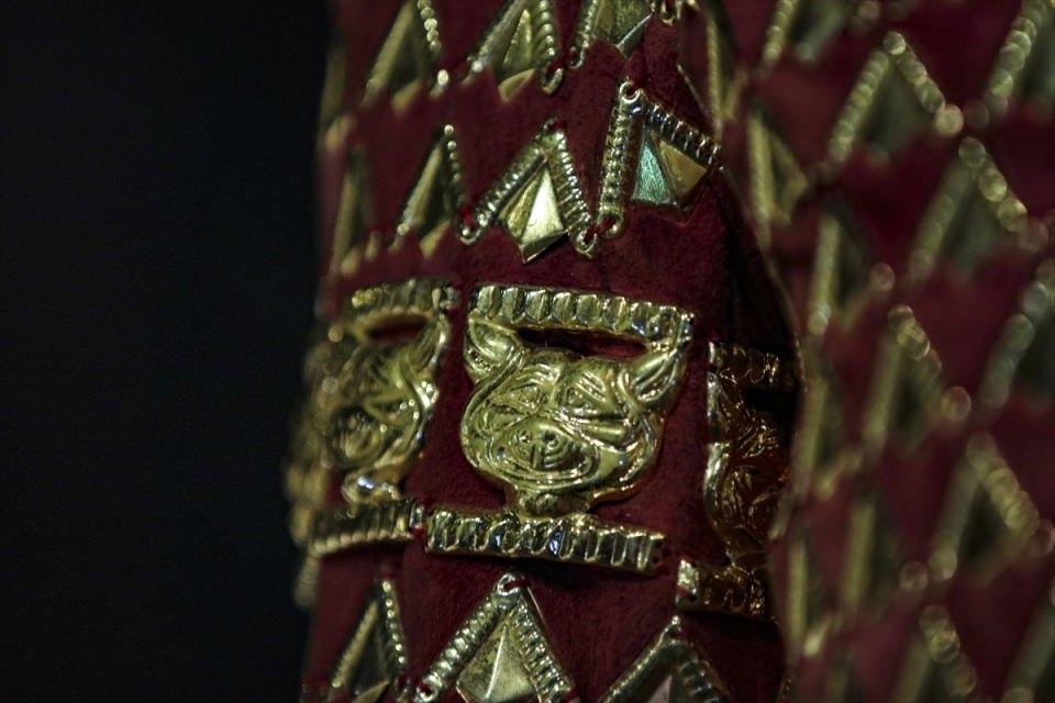 <p>Sağdan sola doğru kapanan V yakalı kısa kaftan, dar süvari pantolonu, diz altında kalan kısa yumuşak çizmeden oluşan zırh, 65 santimlik kalpağıyla dikkati çekiyor. Ucunda dağ keçisi motifi bulunan kalpakta, dünya hakimiyetini simgeleyen 4 okla güneş tanrısını sembolize eden 2 kanatlı at motifi dikkati çekiyor. </p>
<p> </p>