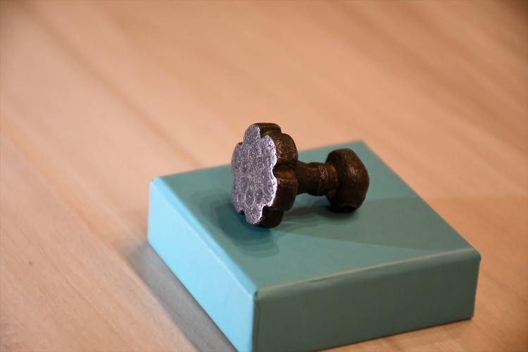 <p>"Baskı kısmı &ccedil;i&ccedil;ek bi&ccedil;imli, yukarı doğru incelen sap kısmı fasetli ve halka kabartma bezemeli, tutamağı &ccedil;eki&ccedil; başlı olarak tanımlanan nikel alaşımlı bronzdan yapılmış 2,7 santimetre y&uuml;ksekliğinde, 2,2 santimetre genişliğinde madeni m&uuml;h&uuml;rd&uuml;r.</p>
