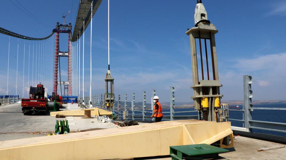 <p><strong>2023 METRE ORTA AÇIKLIĞIYLA DÜNYANIN EN UZUNU OLACAK </strong></p>
<p>1915 Çanakkale Köprüsü, tasarımındaki inceliklerle de dünyada ilk olmaya aday. Cumhuriyet’in 100'üncü kuruluş yıl dönümünü temsil eden 2023 metrelik orta açıklığıyla köprü tamamlanınca 'dünyanın en büyük orta açıklığına sahip asma köprüsü' unvanına sahip olacak. 1915 Çanakkale Köprüsü'nün kule bağlantıları ve bağlantı unsurları, Türk bayrağının renkleri olan kırmızı beyaz olacak. 318 metrelik yüksekliğiyle Çanakkale Deniz Zaferi'nin kazanıldığı tarih olan 3'üncü ayın 18'ini simgeleyen kulelerin üst kısmı da Seyit Onbaşı'nın Çanakkale Savaşları'nda namluya sürdüğü top mermisini temsil edecek şekilde olacak. 770'er metre kenar açıklıklarla toplam 3 bin 563 metre uzunluğundaki köprü, 365 ve 680 metrelik yaklaşım viyadükleriyle birlikte toplam 4 bin 608 metre geçiş uzunluğuna sahip. Gidiş ve geliş yolu 3'er şeritli olan köprü 45,06 metre genişlikte. Köprü tabliyesinin iki tarafında bakım onarım amacıyla kullanılacak yürüme yolları yer alıyor.</p>
<p> </p>