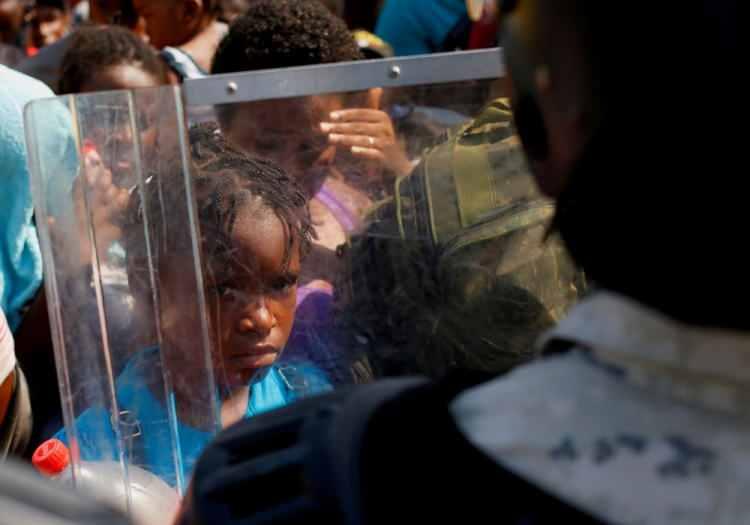 <p>25 Kasım’da Meksika'nın Tapachula kentindeki bir stadyumda, Meksika hükümetinin topraklarından geçmek üzere olan göçmenlerin otobüslere binmek için sıraya girerken Ulusal Muhafız üyesinin kalkanının içinden bir göçmen çocuk görülüyor.</p> <p> </p> 