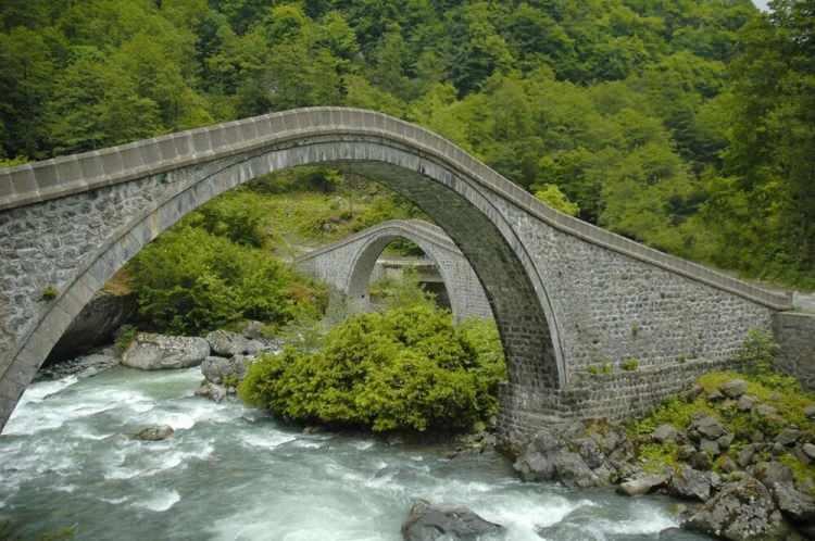 <p><strong>ÇİFTE KÖPRÜLER </strong></p>
<p>Artvin'in Arhavi ilçesinde yer alan ve birbirini tamamlayarak tam daire özelliği taşıyan tarihi "Çifte Köprüler", asırlara meydan okuyan ihtişamlı görüntüsüyle görülmeye değer yerler arasında. Ziyaretçelerin her mevsim yoğun ilgi gösterdiği bu tarihi köprü, kentin en önemli kültürel yapıları arasında gösteriliyor. İlçeye Bağlı Ortacalar bölgesinde Kamilat ve Soğucak dereleri üzerinde birbirini tamamlayayarak konumlandırılan köprüler, 18. yüzyılda moloz ve kesme taşlarla Osmanlı mimarisi şeklinde inşa edilmiş ve yıllar önce restore edilerek turizme kazandırıldı. Yemyeşil doğası ve göz alıcı mimarisiyle görülmeye değer Çifte Köprüler’i rotanıza eklemeyi unutmayın.</p>