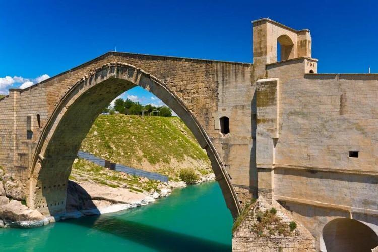 <p><strong>MALABADİ KÖPRÜSÜ </strong></p>
<p>Diyarbakır’ın Silvan ilçesinde yer alan Malabadi Köprüsü, bölgenin önemli tarihi miraslarından biri. Artukoğulları Dönemi'nde Timurtaş Bin İlgazi Bin Artuk tarafından inşa ettirilen köprü 12'nci yüzyıl Selçuklu Dönemi anıtsal mühendislik ve mimarlık başyapıtları arasında. Malabadi Köprüsü, aynı zamanda dünyanın bugüne ulaşan en büyük kemer açıklığına sahip taş kemer köprüsü. Kemerin her iki yanından kervan ve yolcular için iki barınak oda bulunuyor. Üzerinde bulunan insan, güneş ve arslan figürlü kabartmalarıyla da özgün ve dikkat çekici yapılar arasında. Diyarbakır’a yolunuz düşerse burayı görmeden dönmeyin.</p>