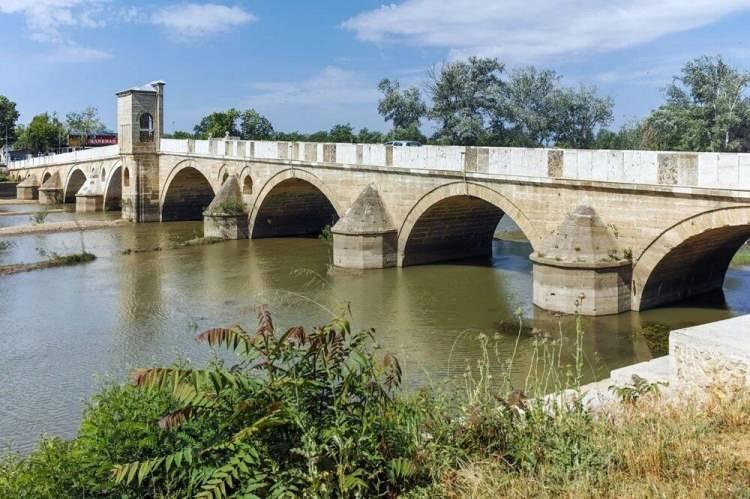 <p><strong>TUNCA KÖPRÜSÜ </strong></p>
<p>Günümüzde Tunca Köprüsü olarak bilinen Ekmekçizade Ahmetpaşa Köprüsü Edirne’nin Odunpazarı ilçesi Tunca nehri üzerinde yer alıyor. 15. yüzyılda Ekmekçizade Ahmet Paşa tarafından yaptırılan köprünün mimarı Sedefkar Mehmet Ağa‘dır. Köprü toplamda 11 ayak ve 10 kemerden oluşuyor. Köprünün bir bölümü ve günümüzde ortada bulunan yazıtlı köşk kısmı su taşkını sonrasında yıkılarak ve 2008 yılında restore edildi. Dikkat çeken mimarisi ve tarihiyle kentin önemli yapıları arasında olan bu köprüyü Edirne’ye giderseniz mutlaka ziyaret etmelisiniz.</p>