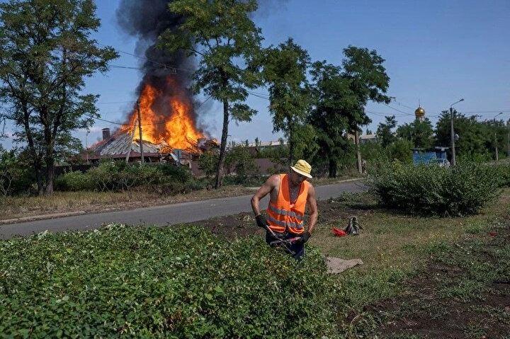 <p>Bir belediye çalışanı, 27 Temmuz 2022'de Rusya'nın Ukrayna'yı işgali sırasında Doğu Ukrayna'nın Bakhmut kentinin varoşlarında bir top mermisinin isabet ettiği yanan bir evin önündeki kaldırımlardaki ağaçları kesiyor.<br />
 </p>
