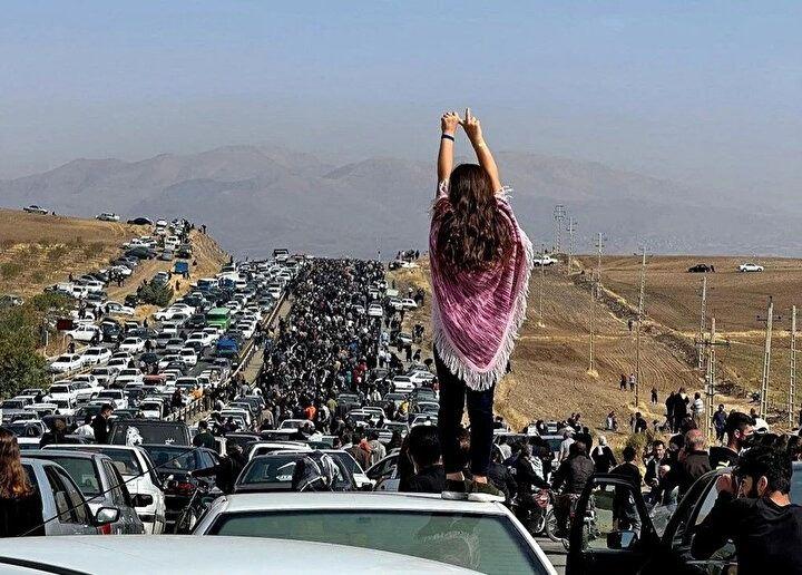 <p>26 Ekim 2022'de Twitter'da paylaşılan bu fotoğraf binlerce kişi gözaltında ölen Mahsa Amini'nin İran'ın batısındaki Kürdistan eyaletindeki memleketi olan Saqez'deki Aichi mezarlığına 40. gün münasebetiyle giderken bir aracın üzerinde duran başı açık bir kadını gösteriyor. 22 yaşındaki Amini'nin Tahran'da ahlak polisi tarafından ülkenin başörtüsü ve tesettür giyime ilişkin katı kurallarını ihlal ettiği iddiasıyla tutuklanmasının ardından 16 Eylül'de ölmesinden bu yana İran'ı bir huzursuzluk dalgası sarstı.</p>