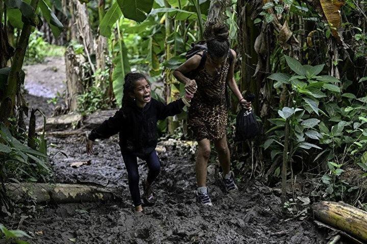 <p>13 Ekim 2022'de Panama'daki Darien Eyaletinin ilk sınır kontrolü olan Canaan Membrillo köyüne vardıklarında Venezuelalı bir göçmen kıza annesi yardım ediyor. Darien Geçidi boyunca yapılan gizli yolculuk genellikle beş veya altı gün sürüyor. Yolculuk her türden tehlikeyi barındırıyor; Kötü hava koşulları: Orta Amerika'ya kokain taşımak için bu yolları kullanan uyuşturucu kaçakçılar, yılanlar, bataklıklar vs.</p>
