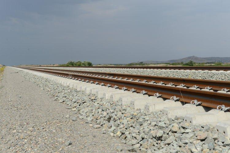 <p>Horadiz-Ağbend demiryolu hattının temeli, 14 Şubat 2021'de Azerbaycan Cumhurbaşkanı Aliyev tarafından atıldı. 110,4 kilometre uzunluğundaki demiryolu hattının güzergahında Horadiz, Mercanlı, Mahmudlu, Soltanlı, Gümlag, Hekeri, Mincivan, Bartaz ve Ağbend isimleri ile 9 istasyon bulunuyor. Ayrıca proje kapsamında 3 tünel, 41 köprü, 7 üst geçit ve yaklaşık 469 yapının inşaatı planlandı. Demiryolu hattının güzergahı boyunca bütün alan mayınlardan temizlendi. İnşaat ve montaj işleri 3 etapta yürütülürken, şu ana kadar demiryolu hattının 38’i tamamlandı. Demiryolu hattı projesinin 2024 yılının ilk yarısında tamamlanması planlanıyor.</p>

