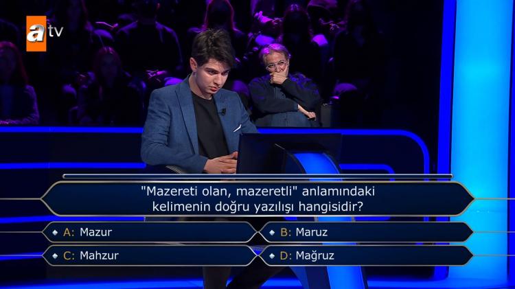 <p><span style="color:#000000"><strong>Karşısına çıkan "Mazereti olan, mazeretli" anlamındaki kelimenin doğru yazılışı hangisidir?" sorusuna yanıt vermekte zorlanan genç yarışmacı, "Mazur", "Maruz", "Mahzur" ve "Mağzur" seçenekleri arasında kararsız kaldı.</strong></span></p>

