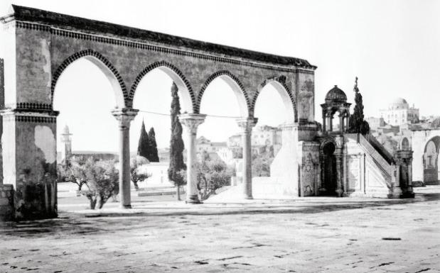 <p><span style="color:#FF0000"><strong>Güney Kanatiri</strong></span></p>

<p>Kubbetüssahra ile Aksa Camii’nin arasındaki güney kanatiri ve hemen yanında bulunan Kadı Burhaneddin Minberi’ni gösteren bu fotoğraf kuvvetle muhtemel 1915 yılı içinde çekilmiştir. Minberin daha sağında, arka planda görülen Tiferet İsrael sinagogunun kubbesi 1900 yılından sonra yapılabilmiştir. Merdivenbaşı kolonlarının revaklarına siyah boya ile yapılmış süsleme de şehrin bir ziyaretçiye hazırlandığını göstermektedir. Enver Paşa’nın 1915 yılı içinde şehri ziyaret ettiği göze alındığında bu fotoğrafın o döneme ait olduğu tahmin edilebilir. </p>
