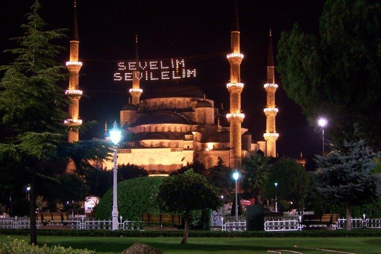 <p>MAHYA NE DEMEKTİR? </p>
<p> </p>
<p>"Aya mahsus" anlamındaki Osmanlıca "mâhiyye" kelimesinin günümüz Türkçesindeki şekli olan mahya, özellikle ramazan aylarında birden fazla minareli camilerin iki minaresi arasına kurulan ışıklı yazı veya resim panosuna verilen addır.</p>
<p>Kelimenin bu anlamı kazanmasında, Hz. Peygamber'e salâtü selâm getirilen zikir meclisi manasındaki Arapça mahyâ kelimesi de etkili olmuştur.</p>
<p>Çünkü kelimeler arasındaki ses benzerliği yanında "leyletü'l-mahyâ" denilen mübarek gecelerde zikir meclisi kurulan camiler alışılmışın üstünde kandillerle donatılmış, hatta mahya tekniğine benzer usullerle süslenmiştir.</p>