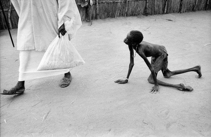 <p>İyi giyimli bir Sudanlı adam, beslenme merkezinin dışında sakat ve aç bir çocuğun elinden mısır çalıyor.</p>