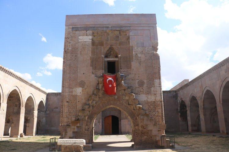 <p><span style="color:#B22222"><strong>KERVANSARAY HAKKINDA</strong></span></p>
<p>Sultanhanı Kervansarayı, Kayseri-Sivas kara yolunun üzerinde ve Kayseri’ye 47 kilometre uzaklıkta bulunuyor. Aynı adı taşıyan mahalle içinde yer alan kervansaray, Selçuklu Sultanı 1’inci Alaeddin Keykubat zamanında 1232-1236 tarihleri arasında yaptırılmıştır.</p>
<p> </p>
<p>Bazı yayınlarda Tuzhisarı Sultan Hanı adıyla da geçen Sultanhanı Kervansarayı, tipik Selçuklu kervansaraylarından biridir. Selçuklu kervansarayları aynı plana göre tasarlanmakla beraber aynı zamanda birbirinden farklı görünüme sahiptirler. Bu fark, ek yapılarla veya unsurlarla belirginleşmektedir.</p>
<p><span style="color:#B22222"><strong>MİMARİ ÖZELLİKLERİ</strong></span></p>
<p>Sultanhanı Kervansarayı da özellikle ortasındaki köşk mescitle görünüm olarak diğer kervansaraylardan ayrılmaktadır. Güney-kuzey doğrultulu kervansaray, plan şemasında 32x45 metre ölçülerinde dikdörtgen planlı kapalı bölüm ve 46x53 metre ölçülerindeki dikdörtgen planlı açık avlulu bölümlerden oluşmaktadır. Kuzey cephesinde yer alan taç kapının tamamına yakını restore edilmiştir.</p>
<p> </p>
<p>Dilimli iki payenin arasına alınmış kapı, geometrik ve bitkisel süsleme bordürleriyle çevrelenmiştir. Az miktarda kalan süslemeden anlaşıldığı kadarıyla kıvrımlı geçme dizisinden sonra 12 ve 8 kollu yıldız sisteminden oluşan geniş geometrik bordür bulunmaktadır. Avlunun ortasında dört kemerli alt yapısıyla köşk mescit yer almıştır. Dıştan 8x8 metre içten yaklaşık 5,30x5,30 metre ölçülerinde kare planlı mescit mekanı 4 ayak üstüne 4 kemerli açıklıktan oluşan altyapı üzerine yerleştirilmiştir. Mescidin köşelerinde her birinin üzeri farklı geometrik desenlerle işlenmiş sütunçeler bulunmaktadır. Altyapıyı oluşturan kemerlerden doğu ve güney yöndekilerin üzerinde pul desenleriyle işlenmiş kıvrımlı gövdeleri, çekik gözleri ve sivri dişleriyle tasvir edilmiş karşılıklı birer ejder yer almaktadır</p>