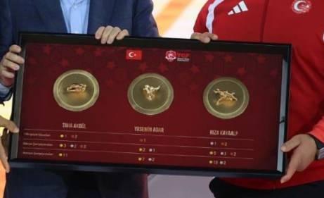 <p>&Ouml;zel olarak tasarlanan eserde; son 15 yılda kazandığı başarılarla T&uuml;rk g&uuml;reşini zirveye &ccedil;ıkaran tarihi başarılar kazanıp rekorlar kıran ağır sıkletin &ouml;nc&uuml; isimleri Rıza Kayaalp, Taha Akg&uuml;l ve Yasemin Adar&rsquo;ın minderlerde en iyi yaptığı ikonik oyunlar betimlenirken, tablonun alt kısmında şampiyonların elde ettiği tarihi başarıların sayısal d&ouml;k&uuml;m&uuml;ne yer verildi.</p>
