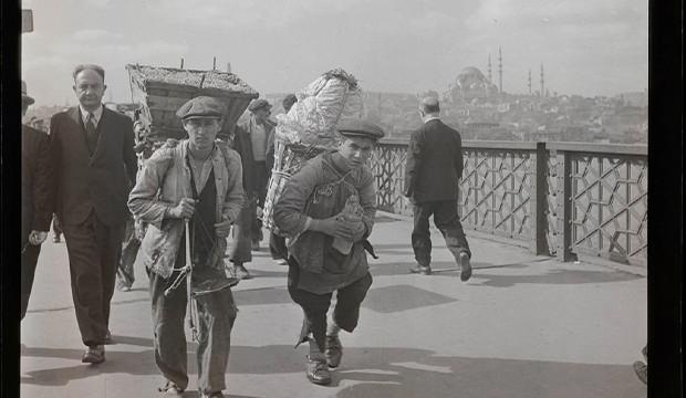<p>Fotoğrafta; Galata K&ouml;pr&uuml;s&uuml;&rsquo;n&uuml;n hareketli atmosferi i&ccedil;erisinde, sırtlarındaki ağır sepetlerle yollarına devam eden iki hamal, şehrin o d&ouml;nemki g&uuml;ndelik yaşamına dair bir kesit sunuyor.</p>
