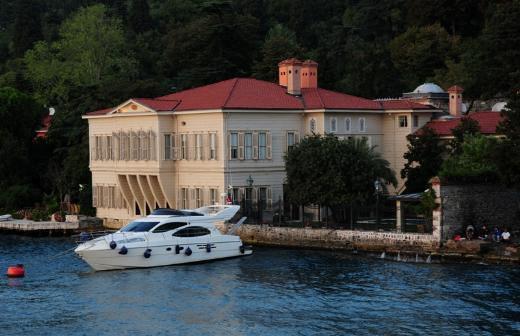 ZARİF MUSTAFA PAŞA YALISI Karadeniz’den Marmara’ya durmadan akan sulara şahitlik yapan Zarif Mustafa Paşa Yalısı, II. Mahmud’un kahvecisi Kani Bey tarafından 1800’lerde satın alınmış. İlk yapıldığında Harem, Selamlık ve Kayıkhane bölümlerinden oluşan ve bugünkünden üç kat daha büyük olan yalı, 1848 yılında Zarif Mustafa Paşa’nın mülkiyetine geçmiş. 1992’ye kadar aynı ailenin fertleri tarafından kullanılmış. Yalı eski bir Bizans manastırının kalıntıları üzerinde yer aldığından Ayazma (Kutsal Su Kaynağı) halen binanın bahçesinde bulunuyor. Paşa’nın damadı Sadık Bey, kayınpederinin sürekli verdiği ziyafetlerden sıkılınca Selamlık ve Kayıkhane olan bölümü satın alıp araya da kocaman bir duvar ördürmüş. Aile Şeyh Talat Efendi’nin akrabasıymış. Sadık Bey’in oğlu Osmanlı mebusu Mehmet Esat Bey yalıda bulunan Hz. Muhammed’in sakalına (Sakal-ı Şerif) ait bir teli Anadolu Hisarı’ndaki Fatih Camii’ne hediye etmiş. Bundan sonra halk yalıyı “Esat Bey Yalısı” olarak adlandırmış. Binanın cihannüması Sakal-ı Şerif’i muhafaza etmek için kullanılmış. 1926’da yalı sakinlerinden Sadiye Hanım’ın düğünü nedeniyle bakımı yapılan bina sarıya boyanınca adı “Sarı Yalı” ya çıkmış. Kurtuluş Savaşı sırasında İstanbul’u İngilizler işgal edince Esat Bey’in oğulları yalıyı Anadolu’ya silah ve mühimmat göndermek için kullanmışlar. Yalının Harem kısmı da İngilizler askerleri için kullanılır kaygısıyla sahipleri tarafından yıktırılmış. Yalı 2000 yılından beri burada oturmakta olan başka bir ailenin mülkiyetinde. Aile Türkiye’nin tanıtımına katkıda bulunmak için elinden geleni yapıyor. Evin zarif hanımefendisi Colin Powell, Oprah Winfrey, Madeleine Albright ve Rus Grand Düşesi Maria Vladimirovna Romanova gibi önemli misafirleri yalıda ağırlıyor. Yalıda bulunan tarihi Türk hamamı güzel bir mermer işçiliğine sahip ve orijinal haliyle muhafaza edilmiş. Binadaki en önemli kısımlardan biri de kadınların deniz hamamı olarak kullandıkları yer. Bunu evin içindeki kapalı bir havuz olarak düşünün. Mahremiyet dolayısıyla geçmişte denize giremeyen kadınlar evin içindeki bu havuzda yüzerlermiş. Şu anda Kahve Odası olarak kullanılan bu yerin camla kaplı zemininin altında balıklar yüzüyor! Günümüzde akvaryum olan bu havuzun filtre edilmiş suyu Boğaz’dan geliyor.