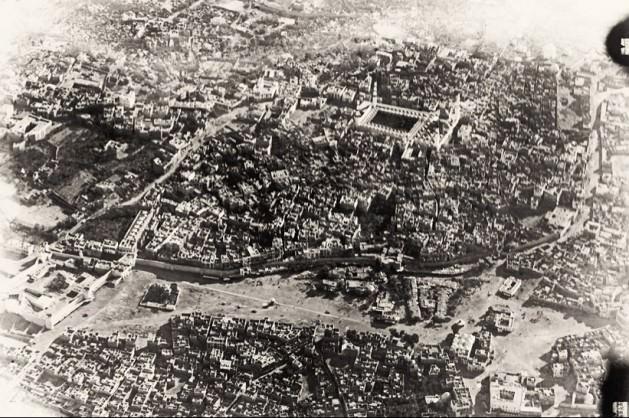 1918’de Medine’nin uçaktan görünüşü. Hazret-i Peygamberin mezarının da bulunduğu Mescid-i Nebevi çevresinde kurulmuş olan Medine de pek çok İslam şehri gibi surlarla çevrilidir. Surların hemen dışında, ortada görülen alan Menaha Meydanı'dır.