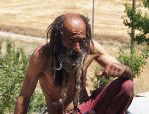 <p>Gözleri de dişleri de çok sağlam. Ancak kesinlikle kimsenin gözünün içine bakmıyor. Eski arkadaşlarından ya da tanıdıklarından birinin öldüğünü duyduğu zaman hemen yerinden kalkıp bir takla atıyor. Niye yaptığını sorduğumuzda ise “Bu da benim onlar için yaptığım ibadetim” diyor. Bir ara sıcaktan bunalıp üstündeki yırtık kazağını da çıkardığında saçı ve sakalı daha da ortaya çıkıyor. Bir gram yağ yok ama öyle bir deri bir kemik durumu da yok. Anlatılanlara bakılırsa 40-50 kiloluk hurdayı kilometrelerce taşıyabiliyor.</p>