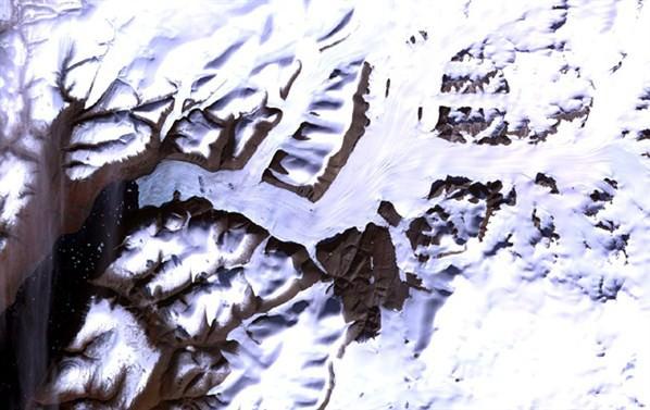 Ellesmere Adası Doğal Park Rezervi Fotoğrafta, Kanada Arktik bölgesinde bulunan Greely Fiyort’undaki, denizden uzanarak oluşan ve buzullara ayrışan yapı görülüyor. Denizin kolu, sol alt köşede göze çarpıyor. Su, buzulun yüzeyinden daha koyu bir renge sahip olduğundan daha fazla ısı topluyor ve erimeyi hızlandırarak giderek büyüyen bir göl halini alıyor.