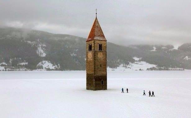 <p>Donmuş bir gölde yükselen kilise kulesi, Reschen, Italy</p>
