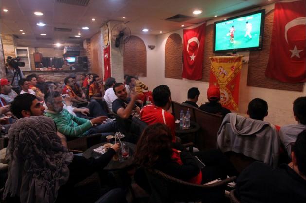 Delicious Cafe'de toplanan taraftarlar, Türk bayrakları ile ekranları başında Galatasaray'ı destekliyor.