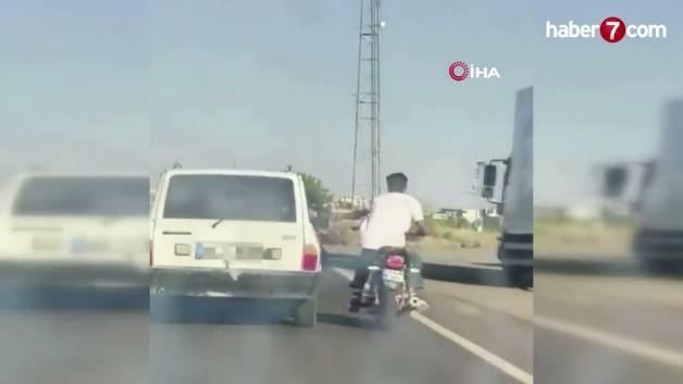 Şanlıurfa Siverek'te bir motosiklet sürücüsünün seyir halindeki otomobilin emniyet kemerine tutunarak ilerlediği an.