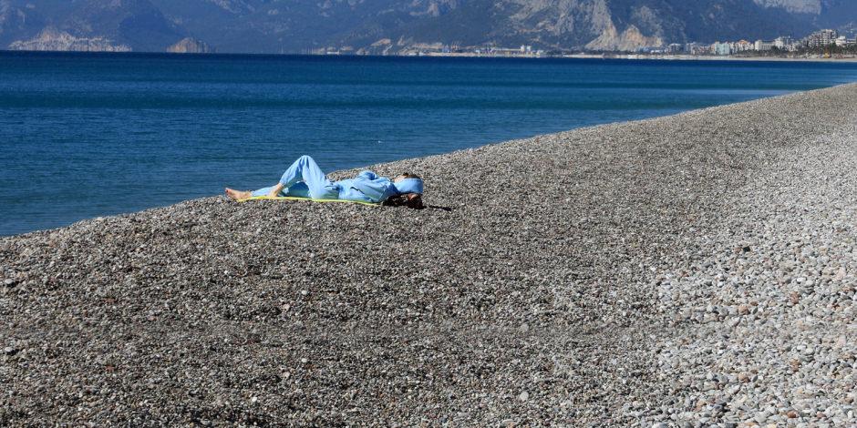 Konyaaltı Sahili'nde eşofmanlarıyla güneşlenen turist