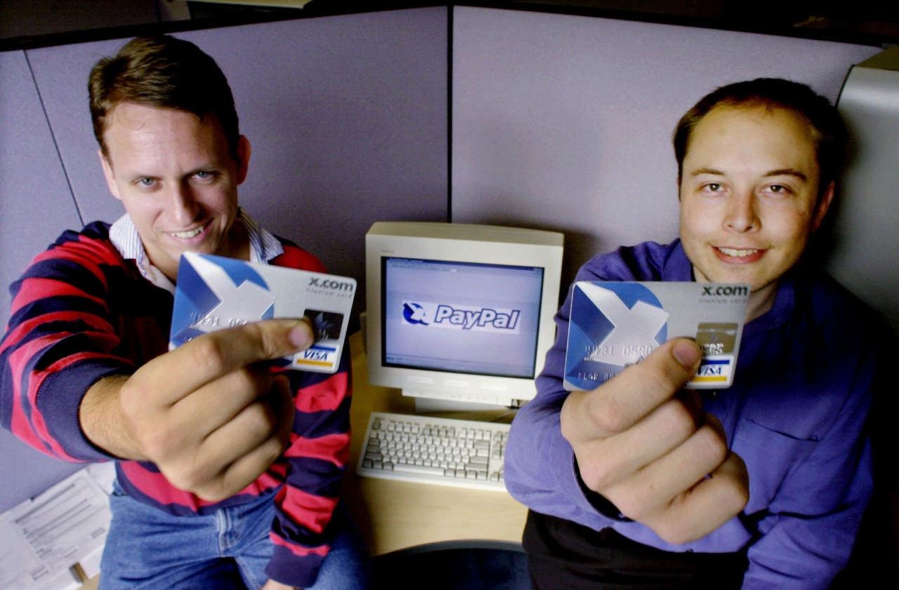 Peter Thiel, solda ve Elon Musk, sağda, 20 Ekim 2000 tarihinde X.com şirket logolu VISA kredi kartlarını tutuyorlar. Paul Sakuma