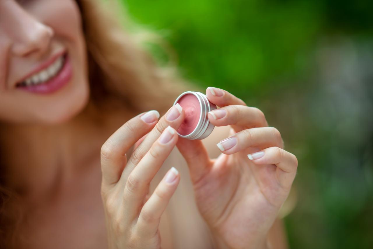 Bir kadın elinde ev yapımı doğal lip balm tutuyor ve gülümdüyor