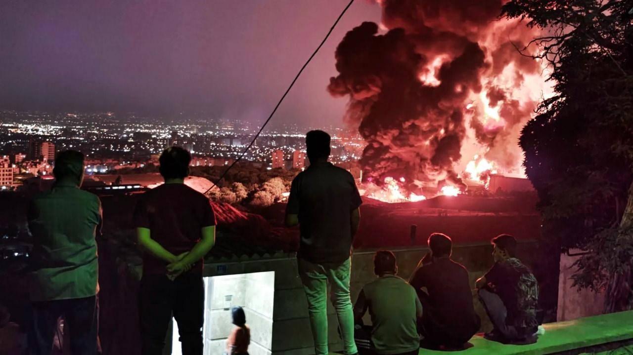 İnsanlar, 15 Haziran 2025′te İran’ın Tahran kentindeki Şahran petrol deposuna düzenlenen İsrail saldırısından çıkan ateşi ve dumanı izliyor.