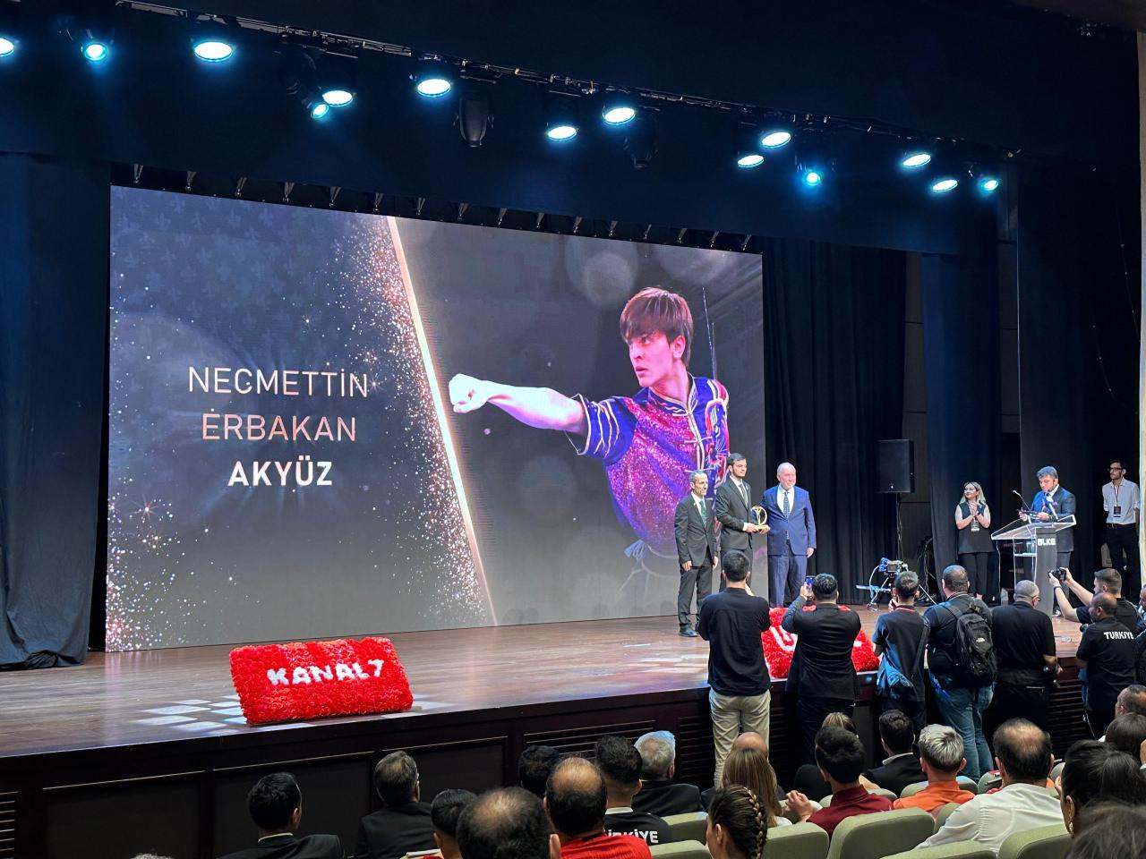 Kanal 7 Yönetim Kurulu Başkanı Zekeriya Karaman, Necmettin Erbakan Akyüz'e plaketini takdim ettiği sıra çekilmiş bir fotoğraf.