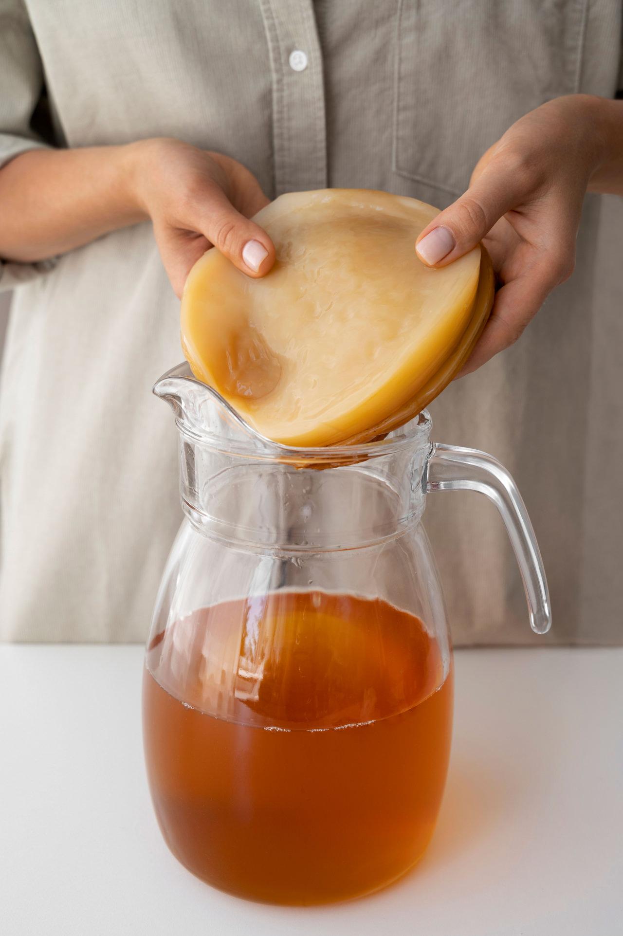 bir kadın kombuchanın içindeki SCOBY'yi gösteriyor.