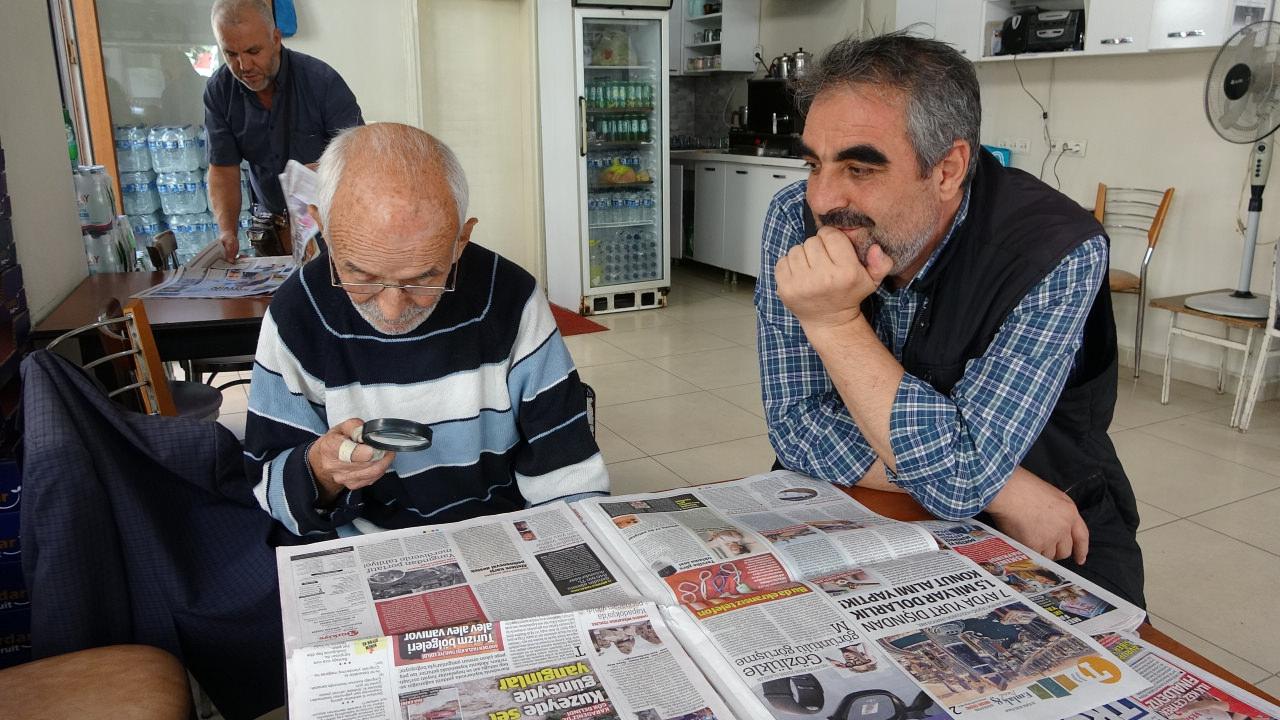 Halil İbrahim Ötegen, büyüteç ile gazete okuyor.
