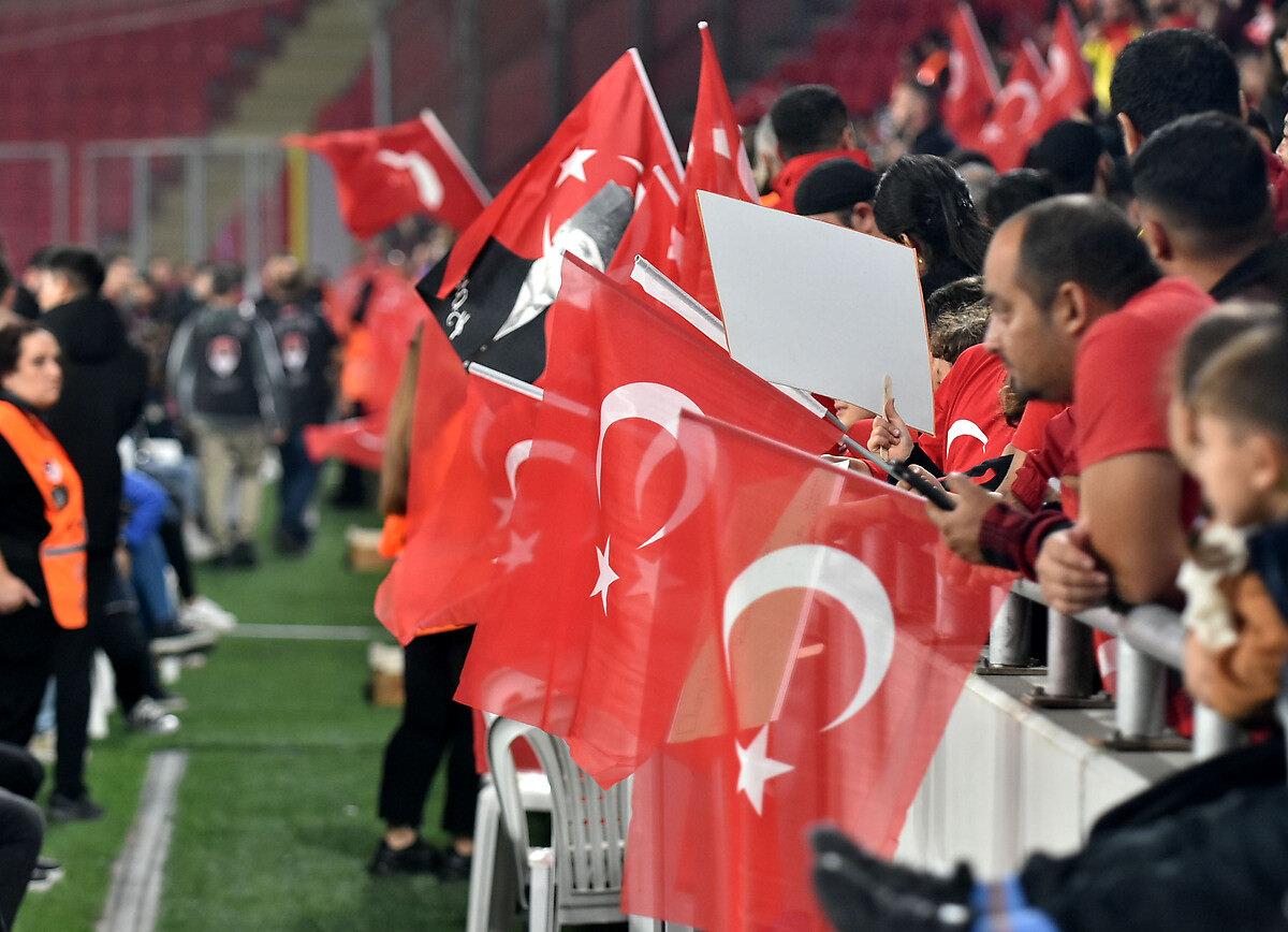 Türkiye'nin oynadığı bir maçta futbolseverler tribünde bayraklarla mücadeleyi takip ediyor.