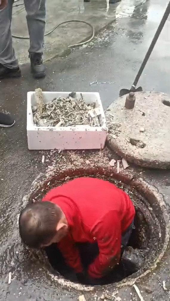 Vatandaş tıkanan kanalizasyonu açıyor.