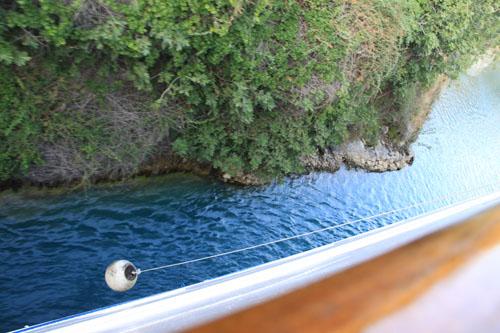 Corinth geçisinde ses dalgalarıyla su iki yana itiliyor. Ocean Majesynin iki yanından sarkan iplere  bağlı bariyerler, geminin sürtünmeden geçmesine yardımcı oluyor.