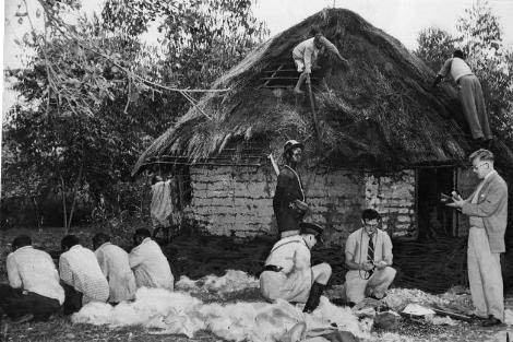 Dört tane Kikuyu çalışanını bir kulübenin dışında tutulurken gösteren fotoğraf.
