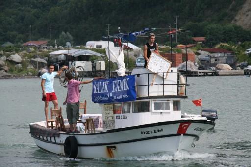 Kastamonu'nun Abana ilçesinde, balık ekmek satan 3 genç, müşteri toplamak ve sahildeki halkın ilgisini çekmek için balıkçı teknesinin arkasına bağladıkları çamaşır ipi ve tahta ile sörf yapıyor.