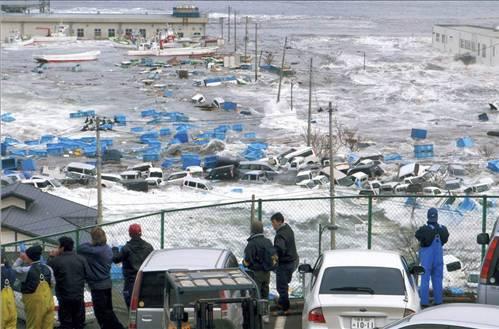 Dalgalara kapılan araçlar: Miyako kentindeki balıkçı limanını vuran 125 metre yüksekliğindeki dev dalgalar, arabaları sürükledi. Olay anında çekilen bu fotoğrafta, felaketten kaçan insanlar yaşananları yüksek bir alandan izliyor.